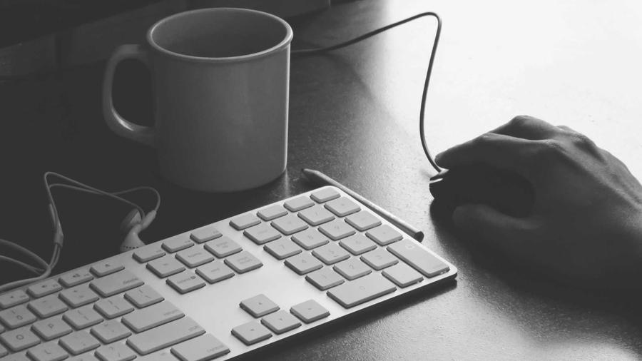 Hand on a keyboard beside a cup of coffee